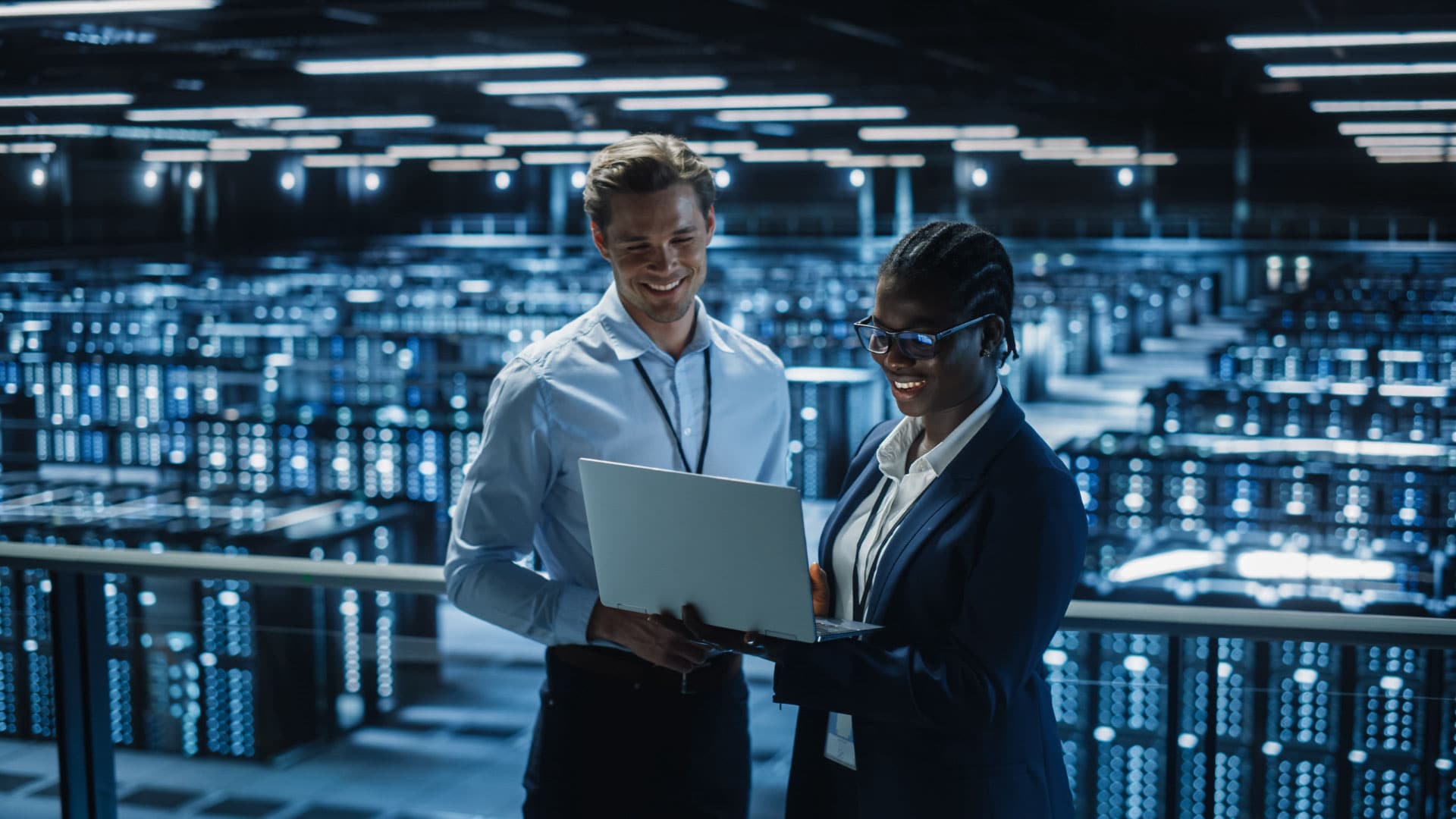 Two People standing in a centre in a data centre looking at a laptop and smiling.