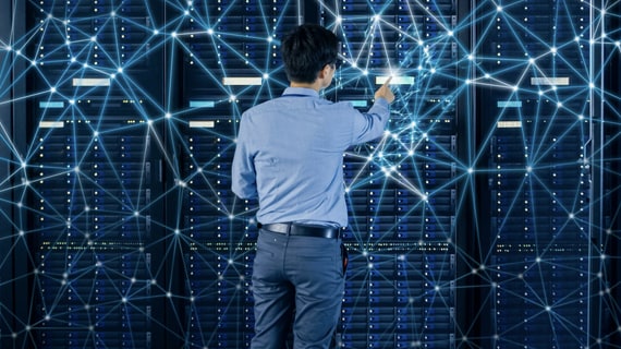 Person standing in data centre looking at a server rack, with a blue coloured representation on a network. 