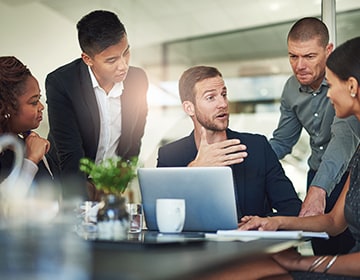 group sitting at a table around a laptop discussing a topic