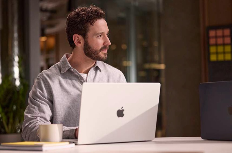 Image of a man working at a desk on an Apple MacBook computer