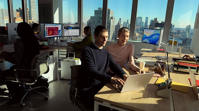 IT professionals working on laptops in modern office managing macOS deployment, security, and device management across enterprise environment