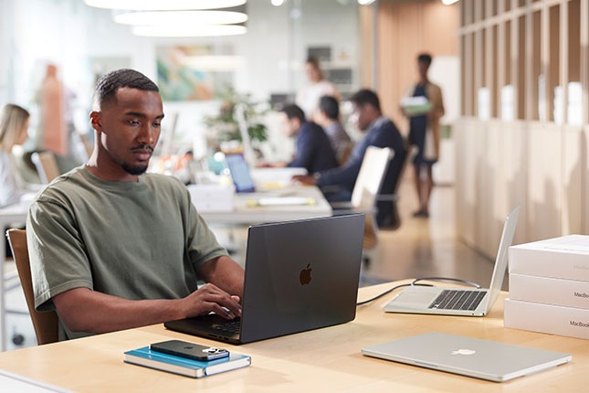 Employee using a MacBook in a modern office, illustrating Apple Business Manager and zero-touch device deployment