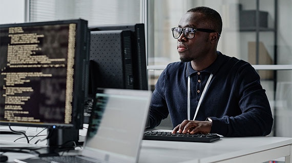 Software developer working at a multi-monitor workstation, building backend services and cloud infrastructure for a supply chain low-stock alert solution.