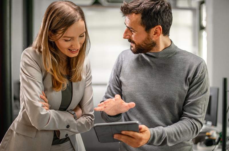 Man and woman in business attire discussing content on a digital tablet in an office.