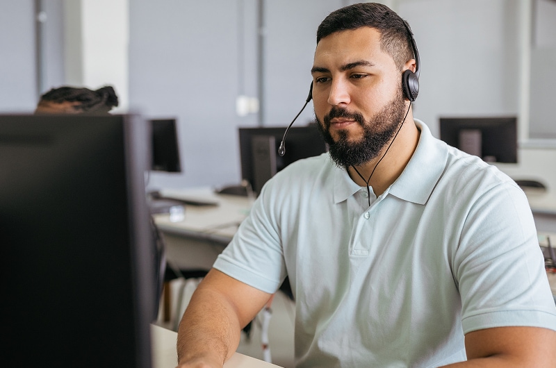 Customer service representative wearing a headset working at a computer in a modern office.