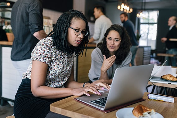 two women working together remotely in a cafe on a laptop