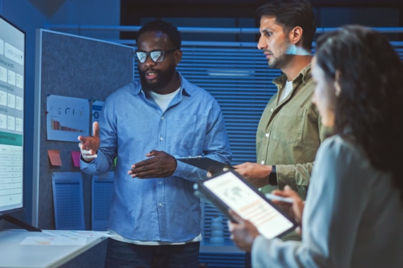 A team of business professionals in front of a large computer monitor.