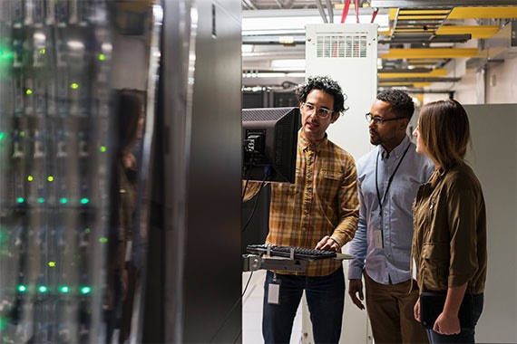 Three colleagues reviewing information on a server room workstation