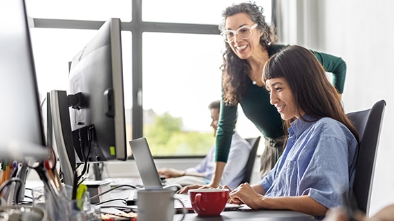 WOmen working together at laptop in bright office.