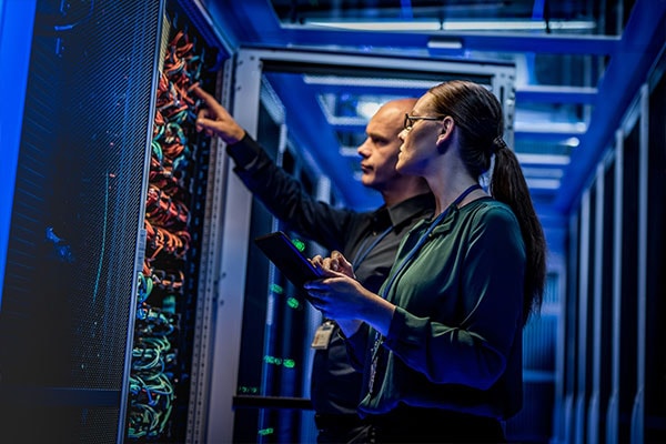 Male IT Specialist Holds Laptop and Discusses Work with Female Server Technician. They're Standing in Data Center, Rack Server Cabinet with Cloud Server Icon and Visualization.