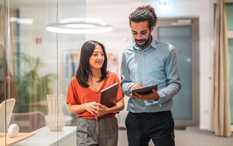 Two professionals collaborating in a modern office, reviewing data on a tablet and notebook—illustrating teamwork and strategy in enterprise data cloud architecture.