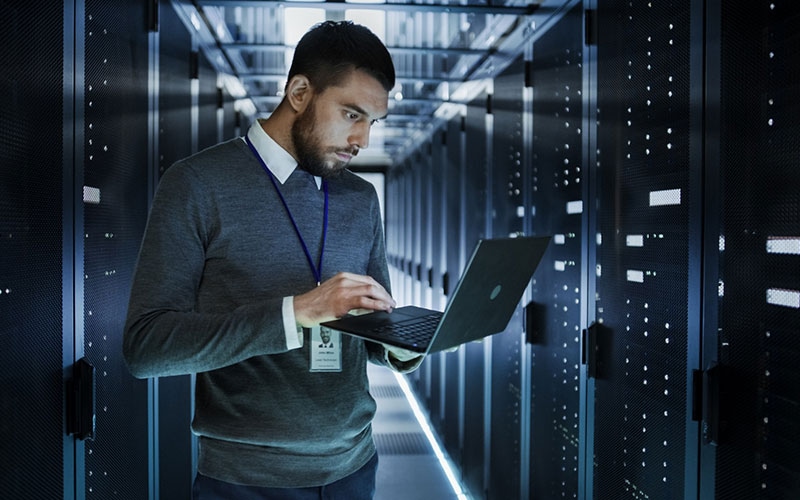 IT professional managing Kubernetes data infrastructure on a laptop in a modern server room—representing Portworx solutions for container data automation, protection, and unification at scale.