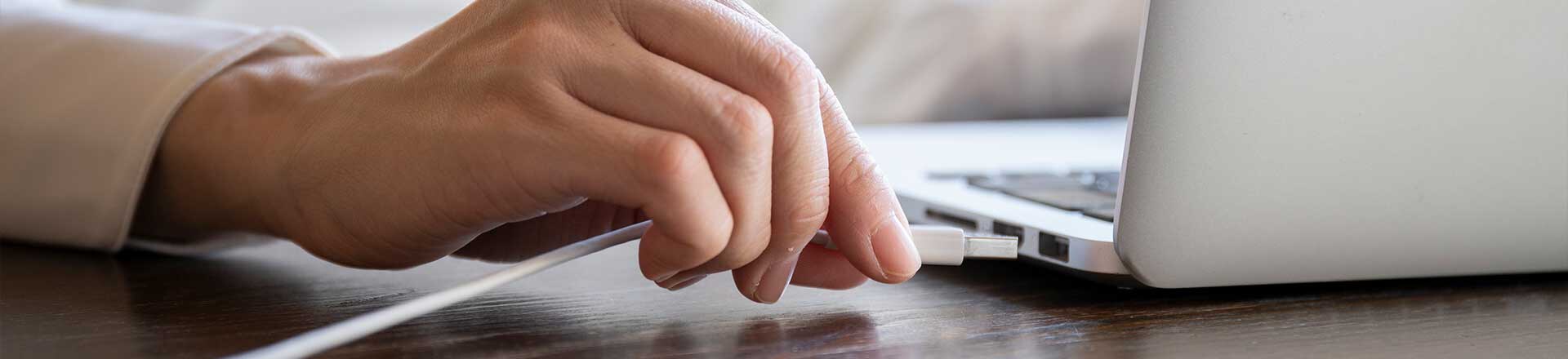 Hand of a woman plugging the cord into the USB of the personal computer