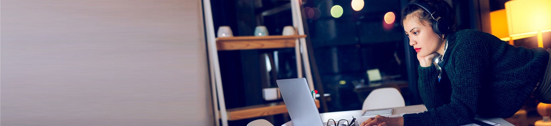 Cropped shot of an attractive young female architect listening to music while using a laptop in a modern office at night