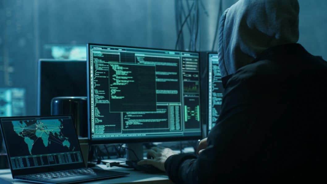Person working on a computer in the dark, (wearing a hoodie, possibly hacking)