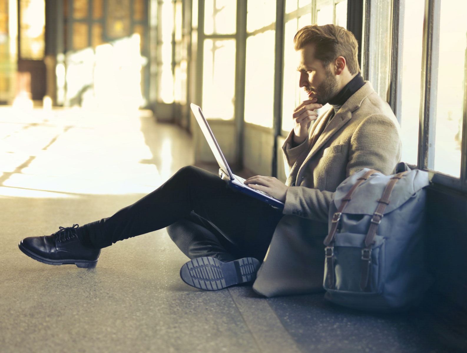 Person sitting on the floor working on his laptop with a confused expression.