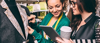  Two women work on a set of cloths and look at an iPad