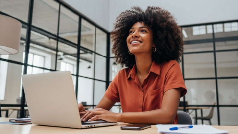 thumbnail image of a smiling woman working on a laptop computer inside an office