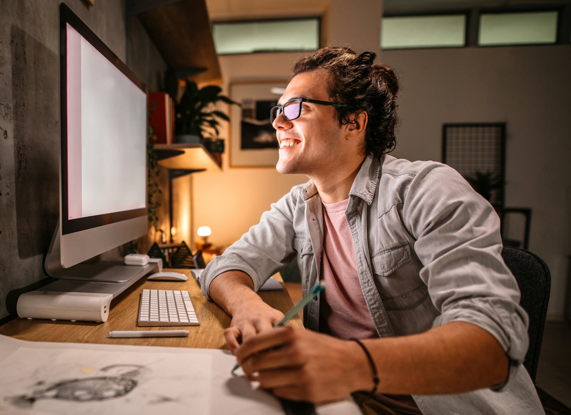 Man working on desktop computer and sketching ideas on paper.