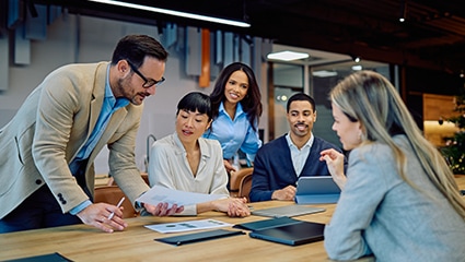 Multiple coworkers in bright office reviewing paperwork.