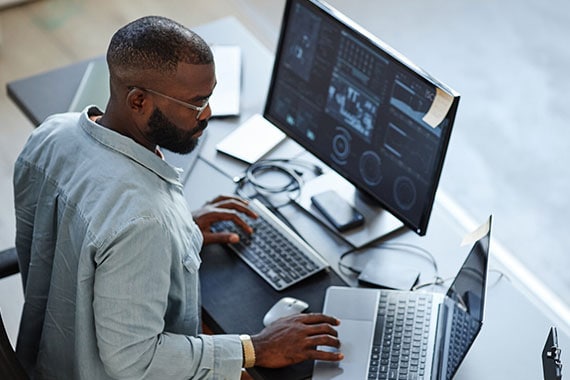 Minimal high angle view at African American software developer working with computers and data systems in office