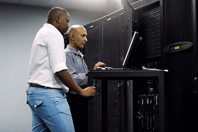 Two IT technicians using a computer while working in a server room.