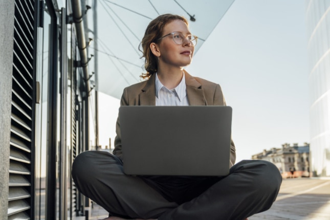 Young business woman working on a laptop outside.