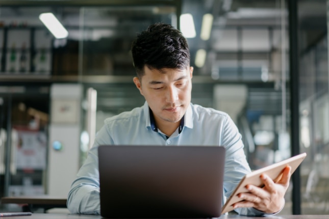 Young man working on multiple devices, a laptop and a tablet.