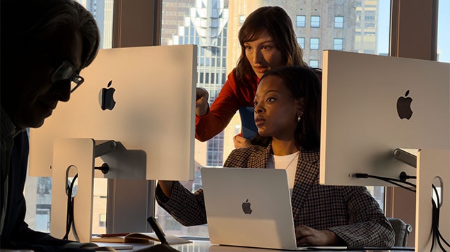 Team members working on Apple iMac and MacBook computers in a modern office workspace.