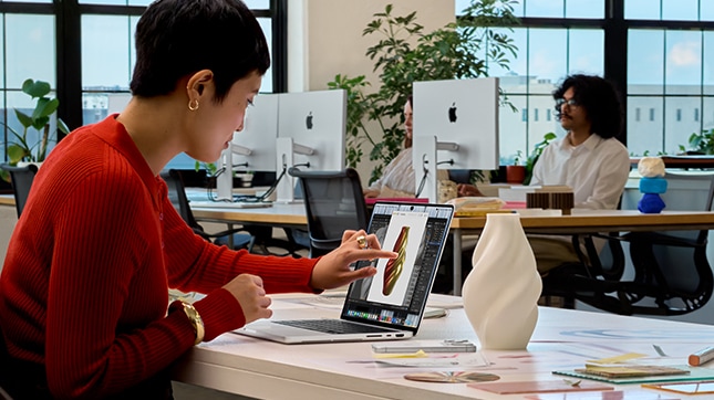 Team members working on Apple iMac and MacBook computers in a modern office workspace.