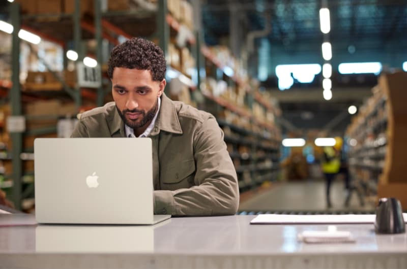 Man working on a MacBook in a warehouse.