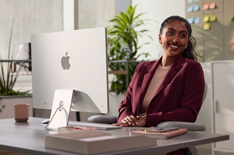 image of a woman sitting at a desk smiling in front of an Apple Computer