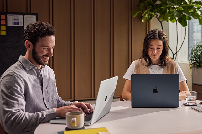 image of two coworkers inside an office working on Apple MacBook computers.