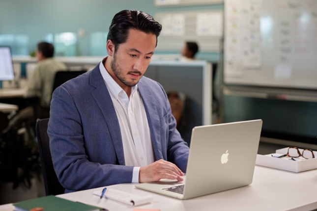 image of a man working at a desk on an Apple MacBook computer