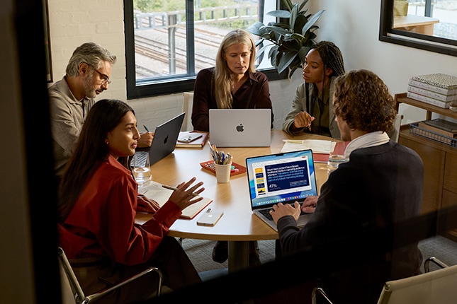lifestyle image of a group of employees working on Apple laptops inside a meeting room
