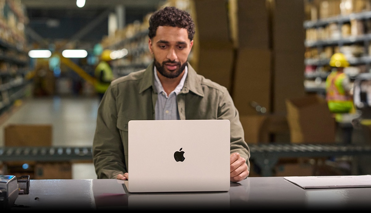 hero image of a man working on an Apple MacBook computer in a warehouse.