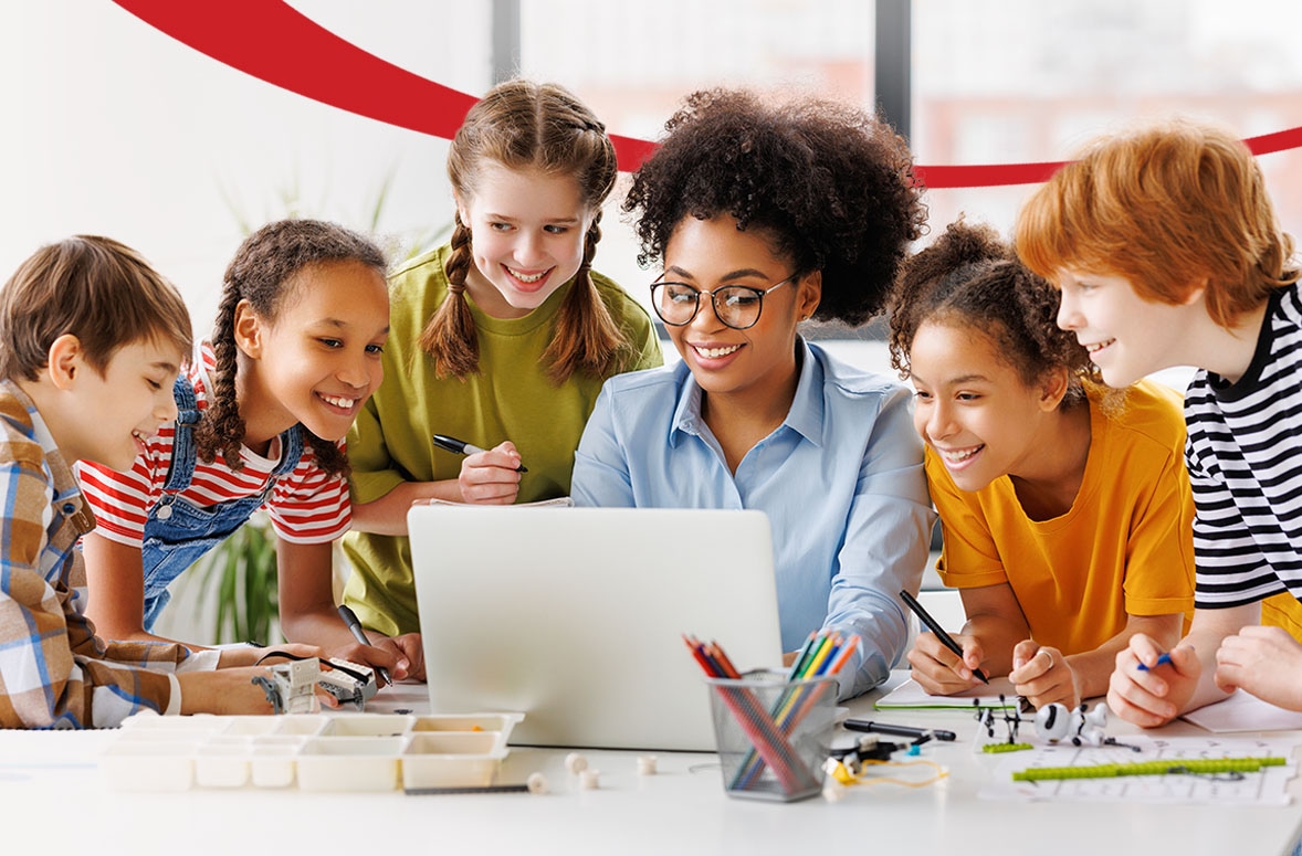 Teacher and two school children smiling and watching educational video on laptop during the lesson in a classroom
