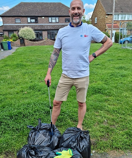 CDW UK coworker stands and smiles next to trash collection bags in a park