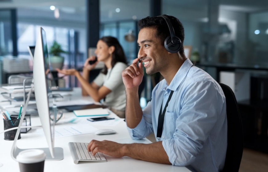 Close up image of a man in a call center with a headset using a desktop computer.