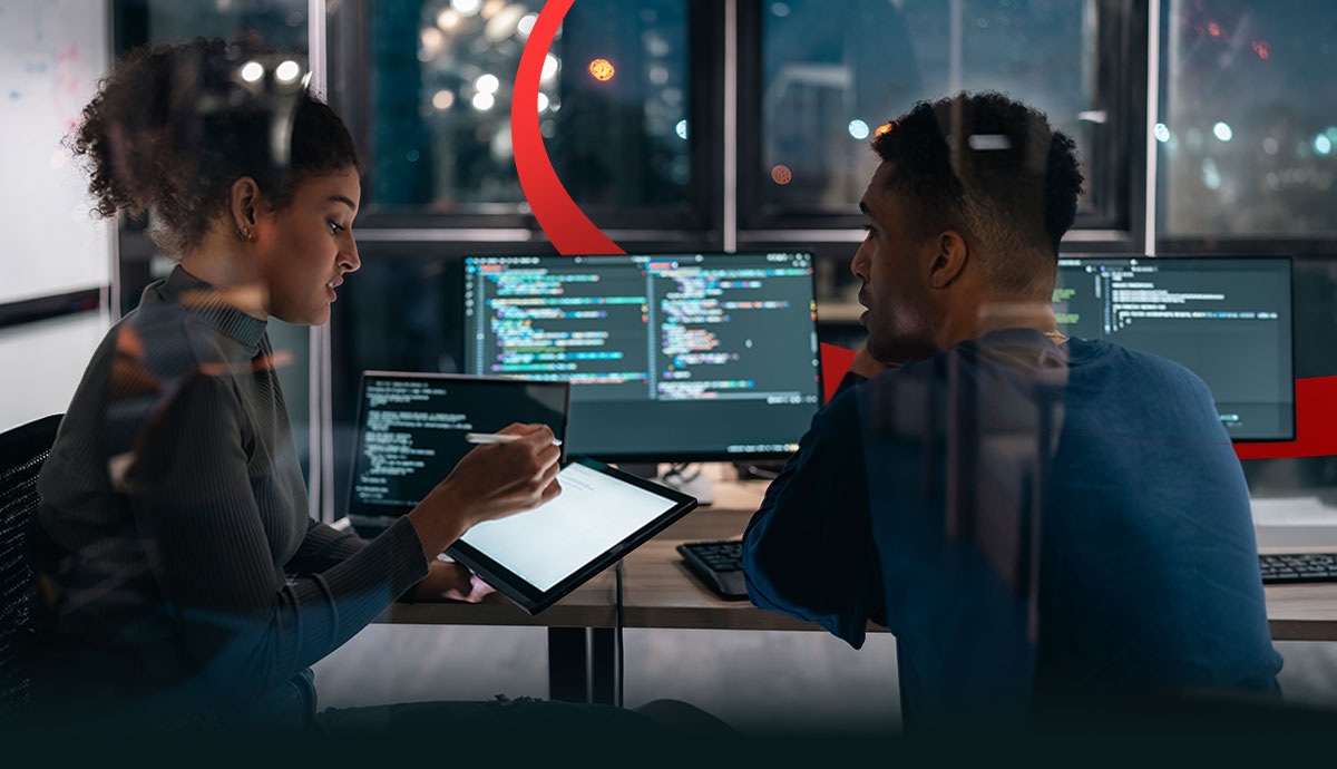 Two software developers reviewing code across multiple monitors in a modern workspace, representing AI-assisted software delivery, code validation, security review, and enterprise software governance with CDW BuildIQ.