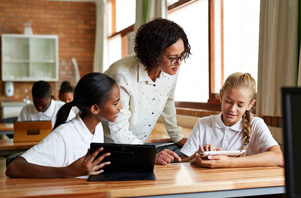 Teacher and two school children smiling and watching educational video on a tablet during the lesson in a classroom