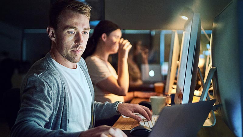 Shot of a young man using a computer and laptop during a late night in a modern office