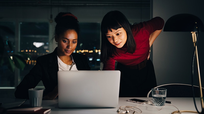 image of two women reviewing data on a shared laptop in an office environment