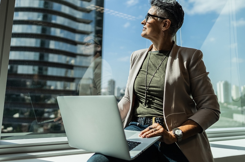 Wide view of a woman using a laptop and looking out the window.