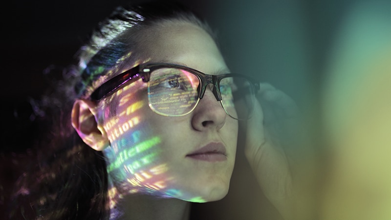 close-up image of a woman reviewing data on a monitor reflecting from her eyeglasses