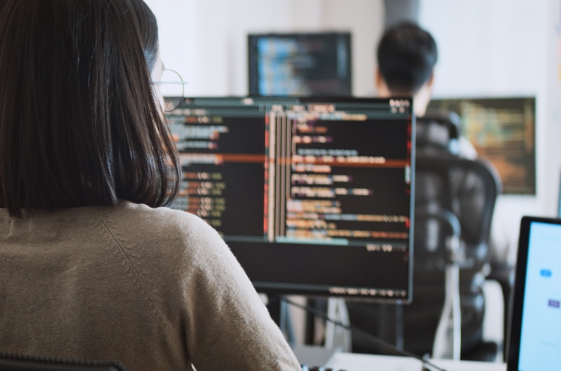 Team coding on multiple monitors in office.