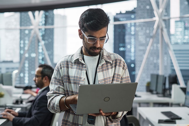 Professional working on a laptop in a modern office with city skyline visible, representing secure and resilient digital operations in a connected world.