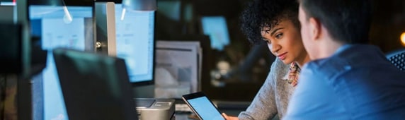 Two people sitting at their desks staring at an iPad