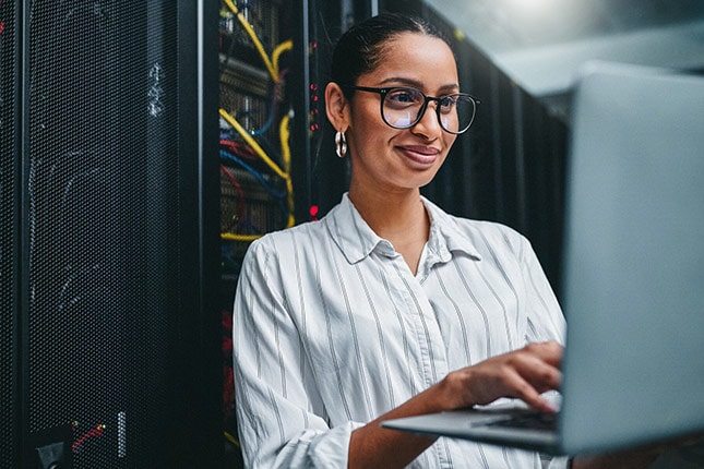 Shot of a young woman using a laptop while working in a server room