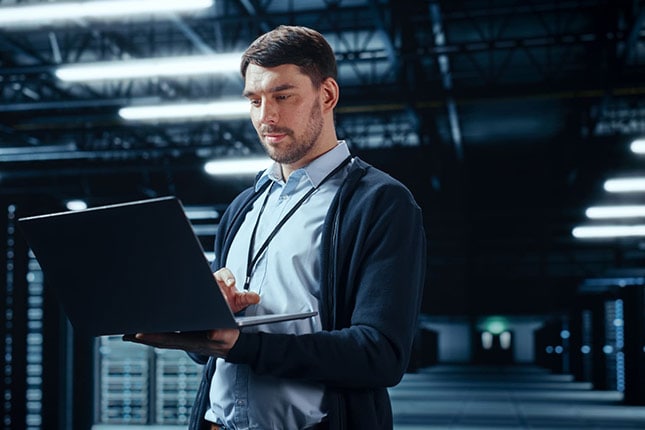 IT Technician in Dark Server Room Holding Laptop